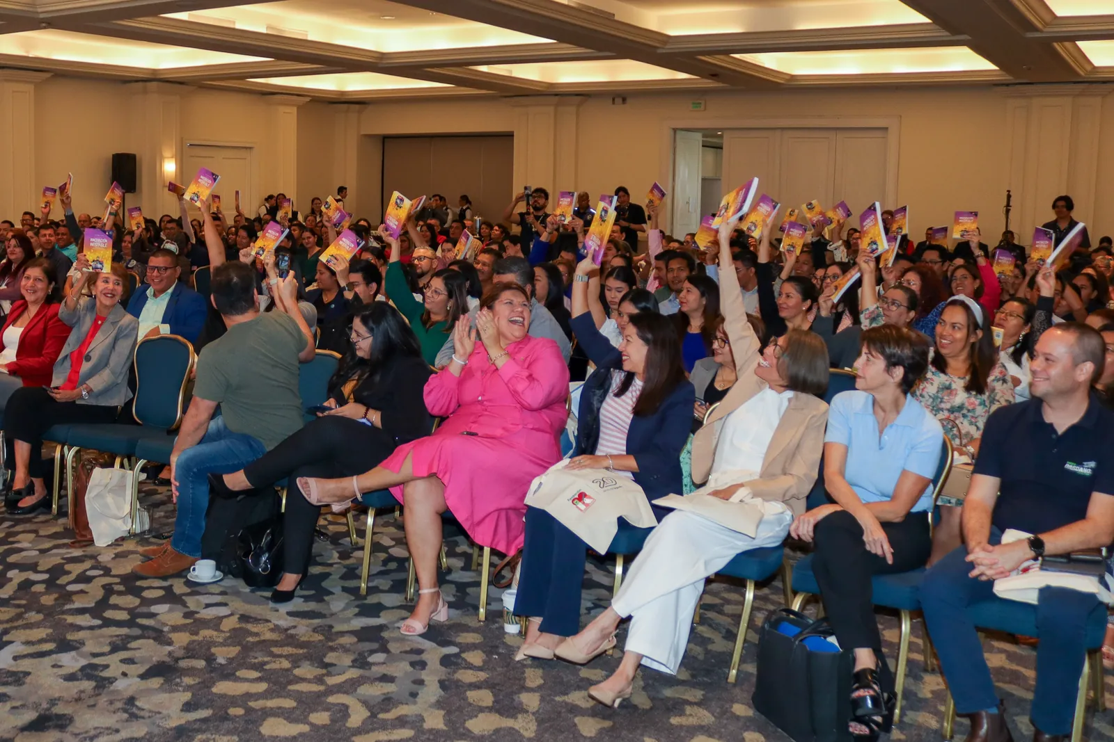 A full room of readers holding up copies of Unstable Innovation at a launch event in El Salvador